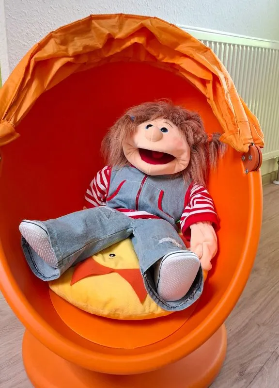 Eine Praxispuppe sitzt im orangen eiförmigen Drehsessel für Kinder Eine Praxispuppe sitzt im orangen eiförmigen Drehsessel für Kinder