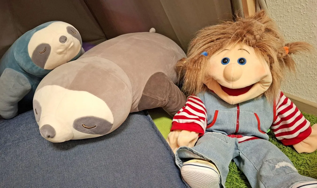 Eine Praxispuppe sitzt mit der Stoff-Faultier-Mama und ihrem Stoff-Faultier-Kind im Spielzimmer-Zelt Eine Praxispuppe sitzt mit der Stoff-Faultier-Mama und ihrem Stoff-Faultier-Kind im Spielzimmer-Zelt