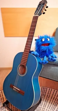 Eine blaue Gitarre steht an einem Sofa, auf dem ein blaues Plüschtier sitzt