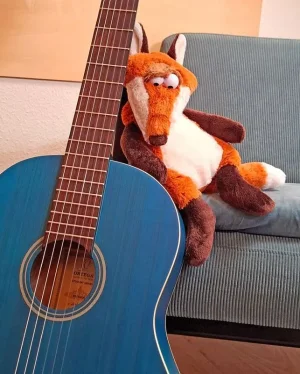 Eine Gitarre steht am Sofa, ein Plüschfuchs lehnt sich an die Gitarre