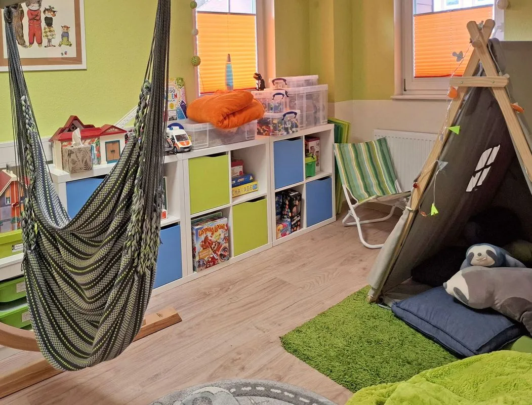 Ein langes Spielzeugregal mit verschiedenem Spielzeug, Hängematte und Zelt im Spielzimmer
