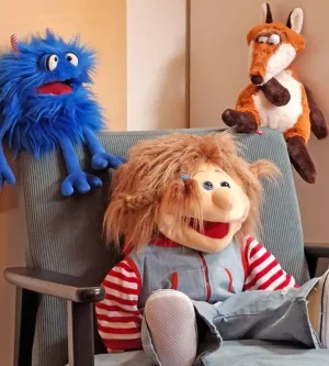 Eine Praxispuppe sitzt im Sessel, ein blaues Plüschtier und ein Plüschfuchs sitzen hinter ihr oben auf der Sessellehne